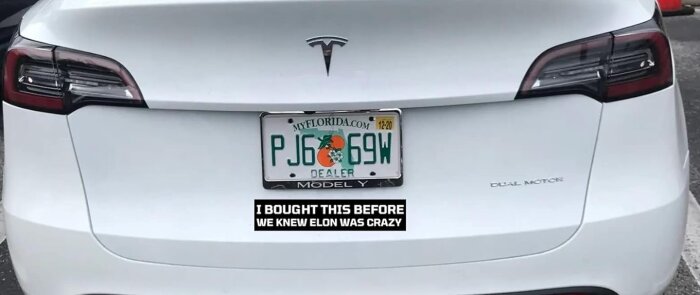 Baksidan av en vit Tesla Model Y med en Floridaregistreringsskylt och en dekal som säger "I bought this before we knew Elon was crazy".