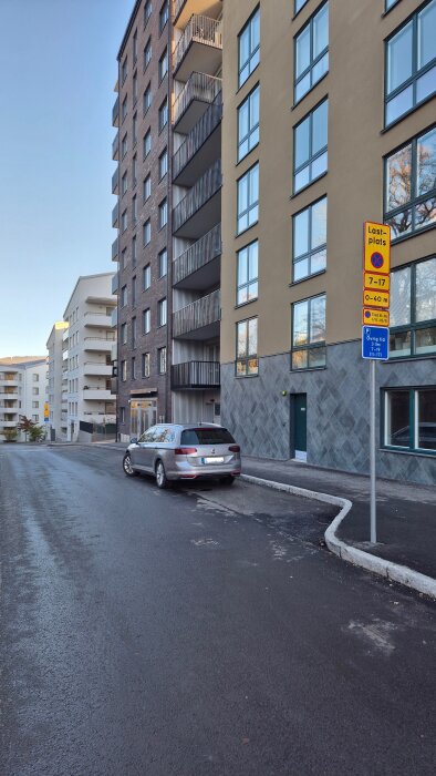 Parkerad bil framför flerbostadshus med lastplats-skyltning, tid 7-17, i urban miljö.