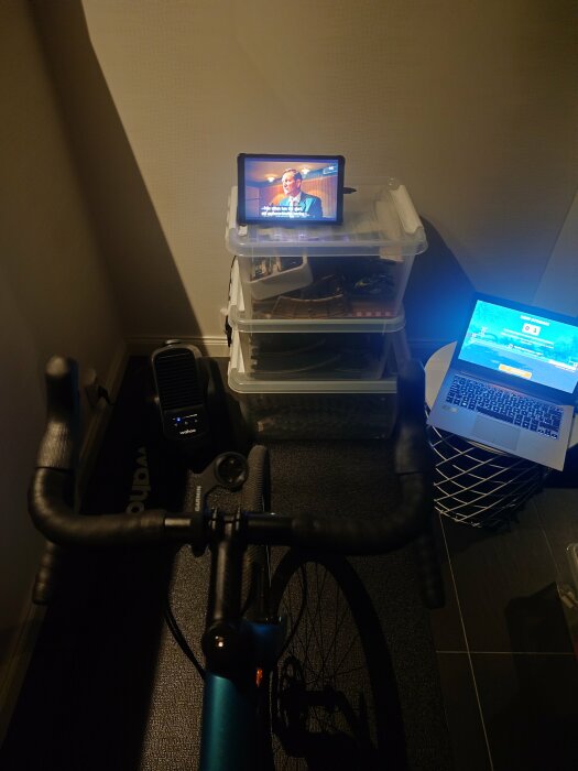 Inomhuscykelstation med surfplatta och TV-program, laptop på sidan och smart trainer.