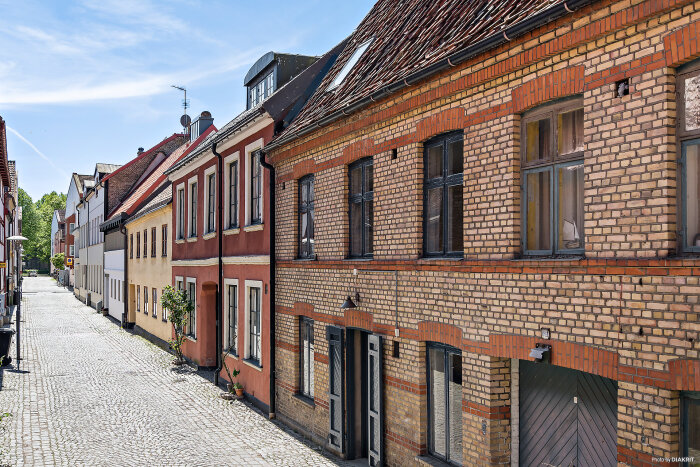 Tegelhusrad i gammal stil längs kullerstensgata i en pittoresk stad. Husen har fönster med träkarmar och röda tegelmönster ovanför fönstren.