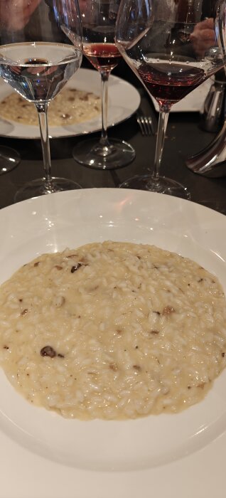 Risotto med tryffel serverad på vit tallrik, omgiven av glas med vatten och rött vin.