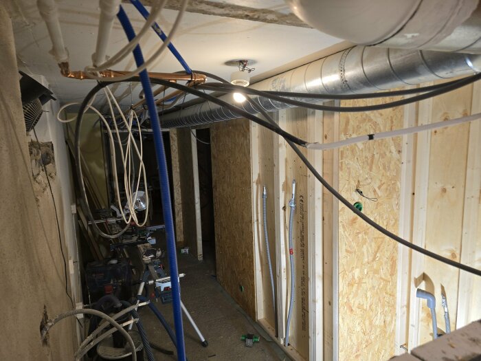 Installation av elledningar och rör i en halvfärdig vägg i tvättstugan. Väggen är öppen med kablar dragna och ventilationsrör synliga.