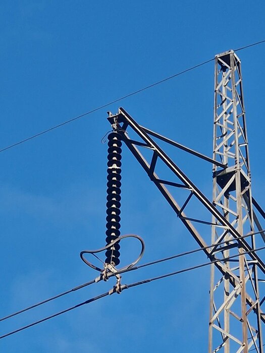 Skadad isolator på kraftledningstorn med blå himmel i bakgrunden.