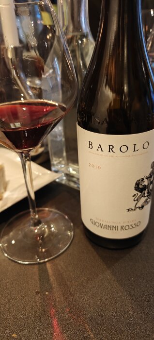 Glas med rött vin bredvid en flaska Barolo årgång 2019, Giovanni Rosso.