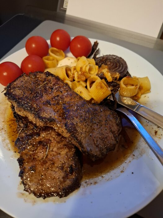 Ryggbiff stekt i smör med pasta, mozzarella, tomater och lök serverad på en tallrik.