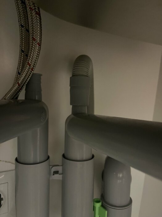 Gråa avloppsrör under diskbänk, en av dem har en plats för eventuell anslutning av diskmaskinens avloppsslang, saknar dock ett hål.