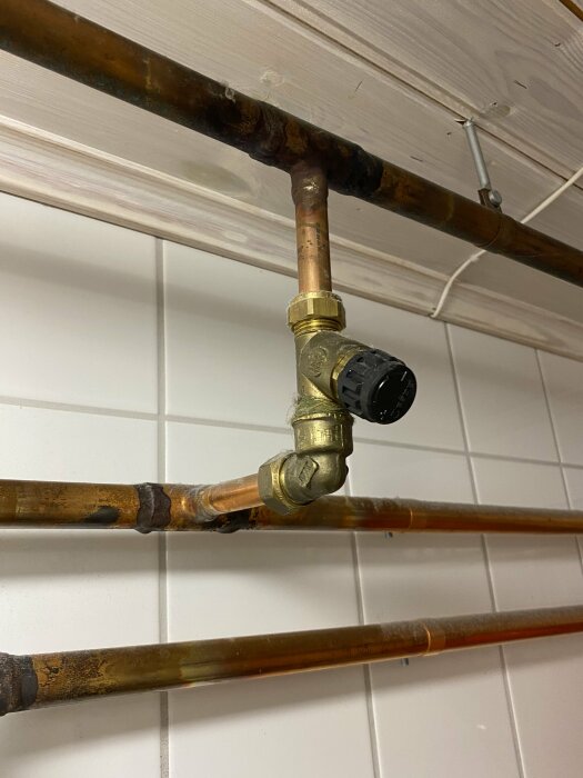 Ventil på kopparrör vid tak, mellan kallvatten och varmvatten, utanför värmepump. Installerad i ett rum med ljus träpanel och kakelväggar.