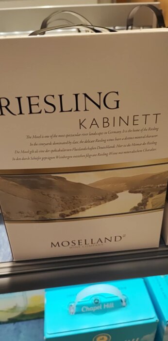 Bag-in-box vin av märket Moselland Riesling Kabinett, med landskapsbild från Moseldalen, uppställt på butikshylla.