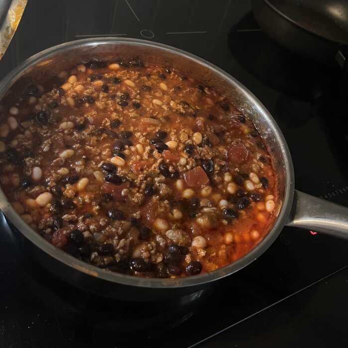 Gryta med köttfärs och bönor i tomatsås på spisen, del av matlagning under en regnig dag.