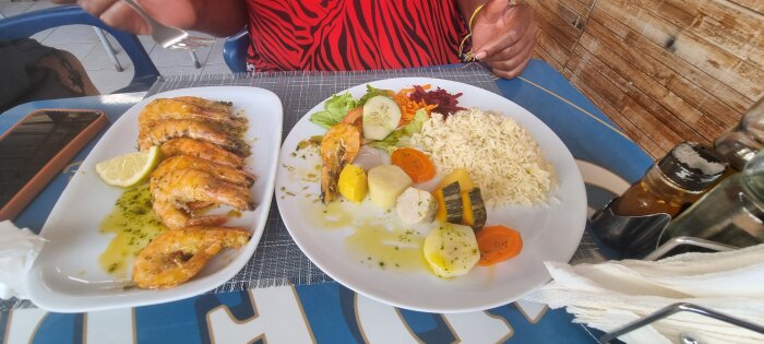 Två tallrikar med skaldjur; den ena med räkor, citron och sås, den andra med bläckfisk, ris, sallad och grönsaker.