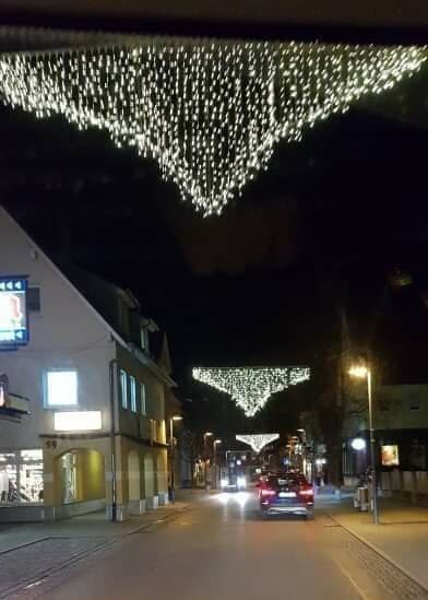 Julbelysning hänger över gata i Trosa, visar en festlig ljusdekoration ovanför bilar i en kvällsscen.