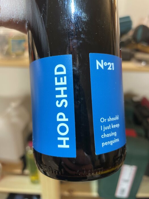 Ölflaska med blå etikett, texten "HOP SHED" och "N°21".