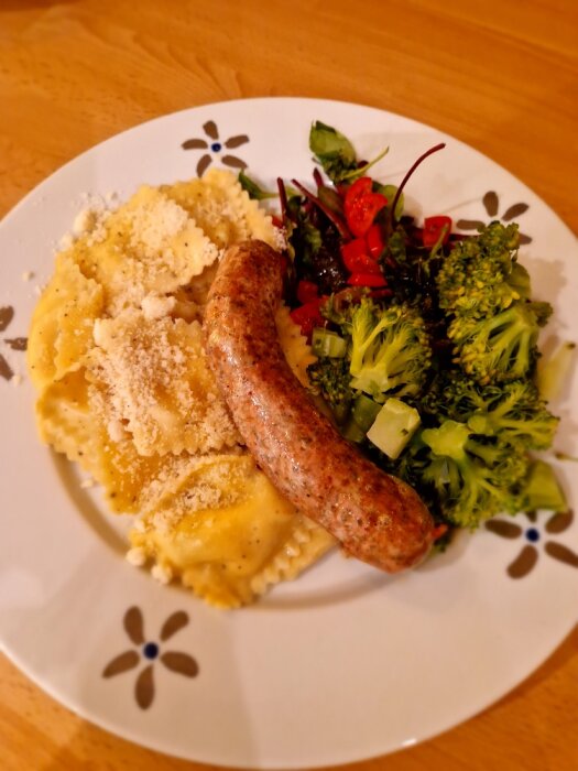 En tallrik med salsiccia, ravioli "cacio e pepe", broccoli och gröna blad på ett bord.