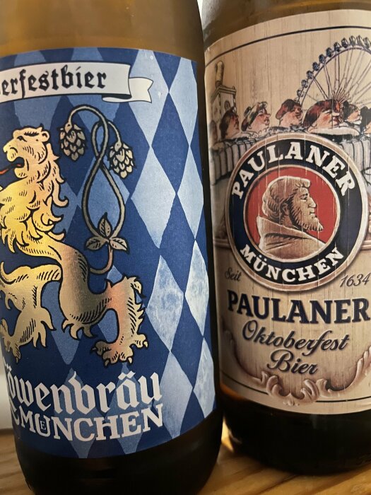 Två Oktoberfestöl med etiketter från Löwenbräu och Paulaner, ståendes bredvid varandra.