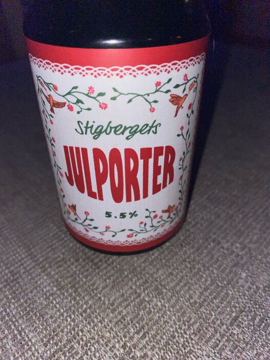 Flaska med etikett "Stigbergets Julporter 5.5%", dekorerad med blommor och fåglar, mot en ljus bakgrund.