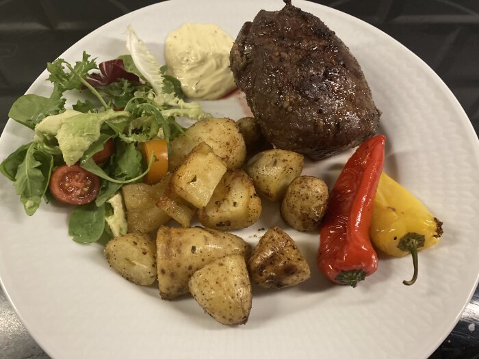 Helgrillad lammrostbiff med ugnsbakade potatisar, grönsallad, tomater och grillad paprika på vit tallrik med en klick sås.