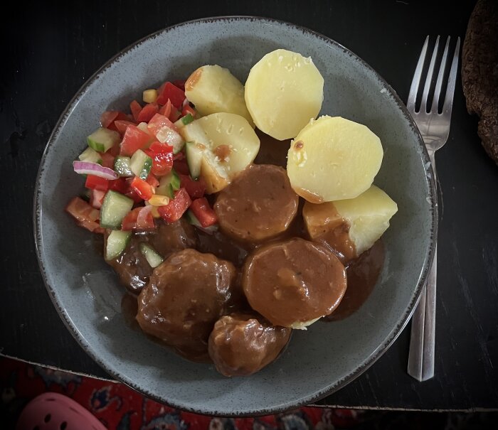 Köttfärsbiffar med sås, kokt potatis och grönsaker på tallrik, serverad med gaffel bredvid.