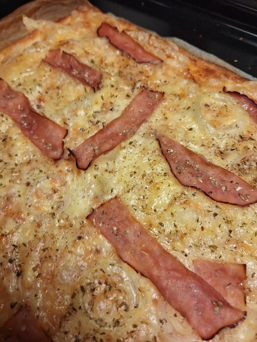 Hemlagad pizza med skinka, tomatsås, ost och lök, toppad med oregano. Skinkan har krympt något vid gräddning.