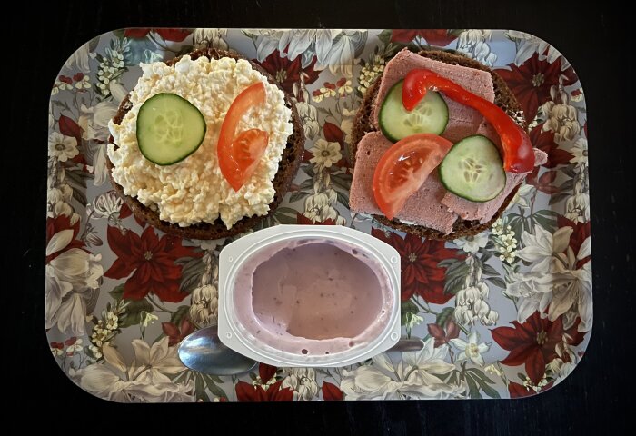 Frukostbricka med två smörgåsar, en med kesoröra, gurka och tomat, en med pastej, gurka, tomat och paprika, samt en skål yoghurt.