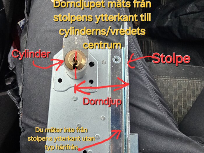 Bild av ett lås med text och pilar som visar mätinstruktioner för dorndjup, cylinder och stolpe.