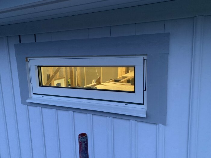 Fönster på garagets övervåning med nyinstallerade plåtar och foder, del av byggprojekt inför isolering och målning.