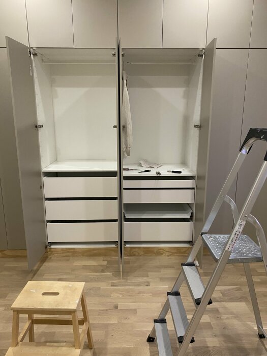 IKEA Metod-stommar med skapade baksidor, två öppna garderober med vita dörrar och lådor, en stegpall framför på trägolv.