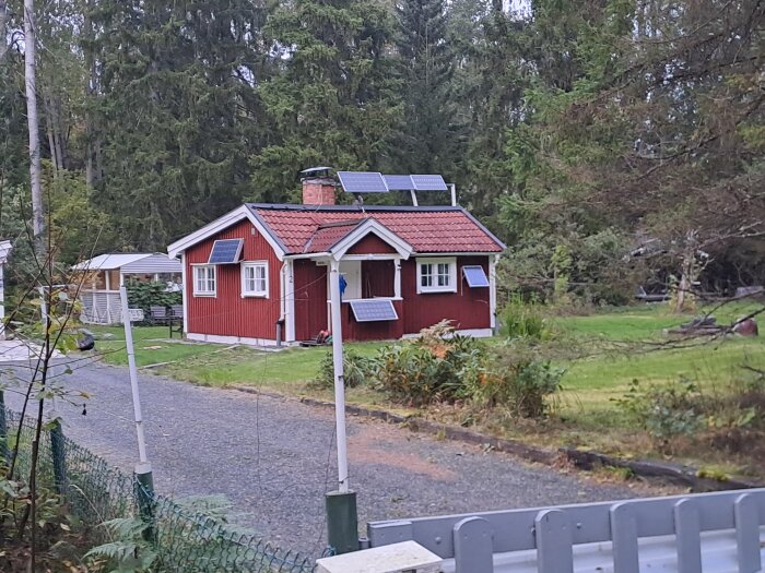 Rött hus med solpaneler på taket och väggen, omgivet av skog och grönska.