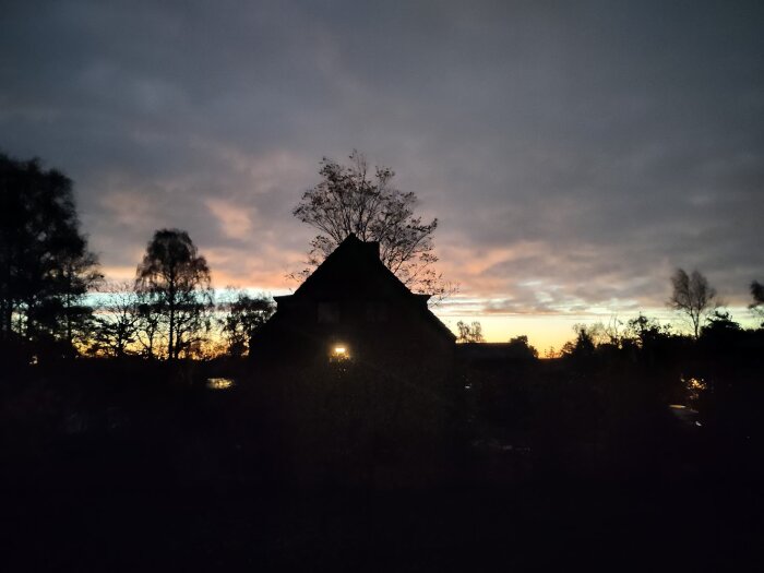 Silhuett av ett hus och träd mot en färgglad solnedgångshimmel.