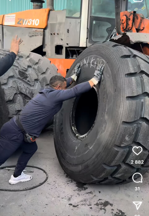 Man byter ett stort traktordäck med orange traktor i bakgrunden.