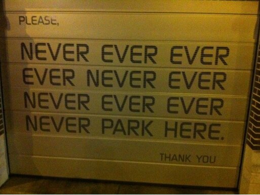 Skylt med text: "Never ever park here" på en garageport.