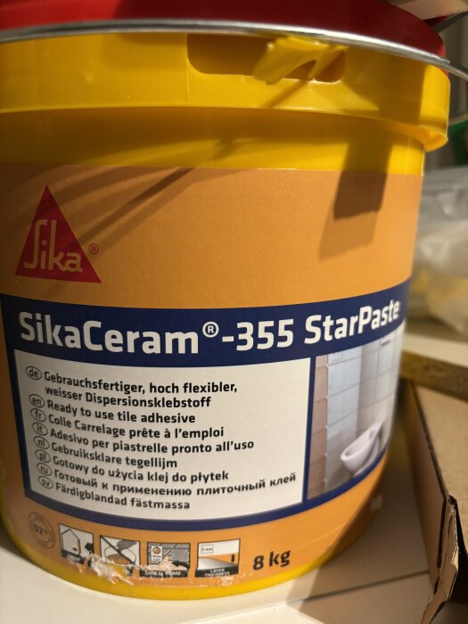 Gul behållare av SikaCeram-355 StarPaste, färdigblandat fix för kakelarbete, står på en vit yta.