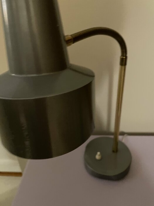 Grå bordslampa med rund skärm och böjd arm placerad på ett bord mot en ljus bakgrund.