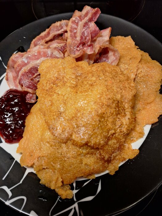 Tallrik med råraka gjord på potatis och morot, serverad med bacon och lingonsylt.