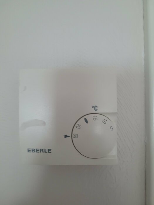 Termostat för uppvärmning märkt Eberle, inställd på cirka 27 grader Celsius på en vit vägg.