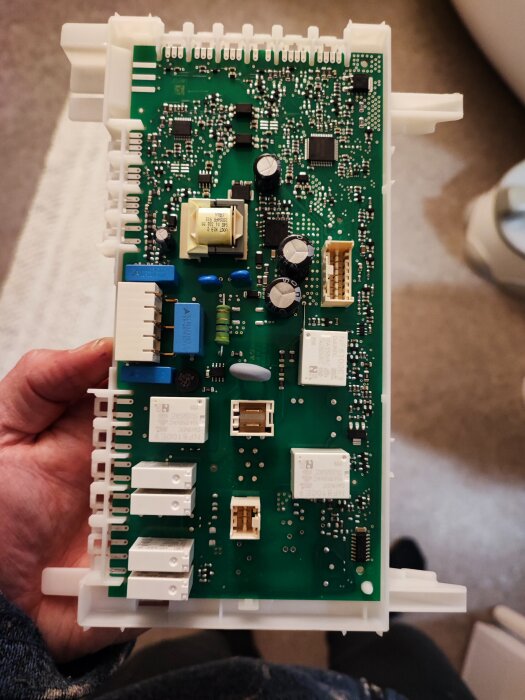 Kretskort från torktumlare med flera komponenter, inklusive vita relämodellen NF8100E9 monterade på kortet.