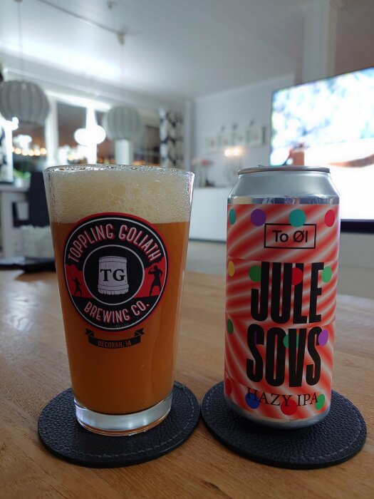 En glas öl från Toppling Goliath Brewing Co. och burken To Øl Jule Sovs Hazy IPA står på ett bord i ett vardagsrum.