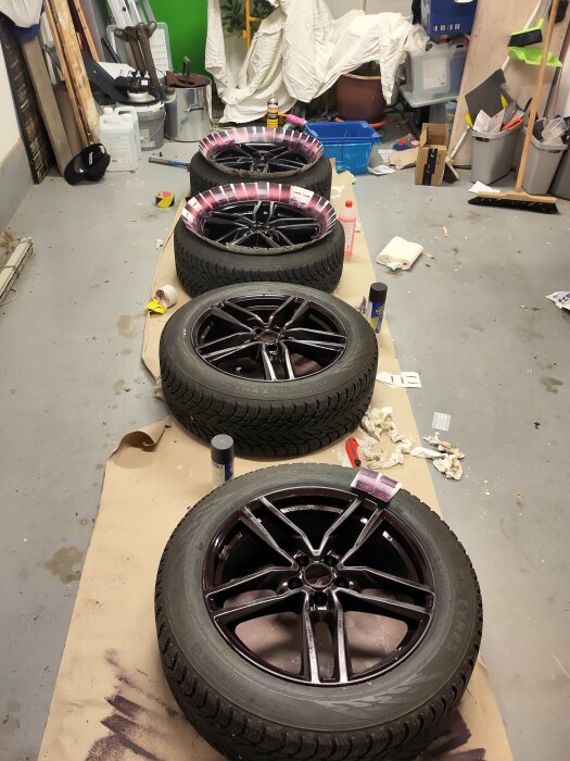 Fyra bildäck med svarta fälgar målade med plastidip blackcherry, placerade i ett förråd med verktyg och material runtom.