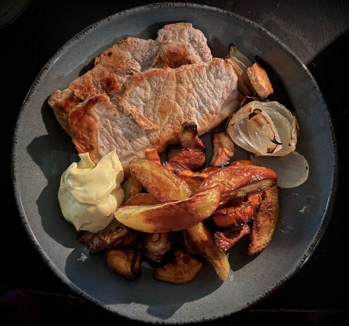 Tunnskuren fläskkotlett med ugnsgrönsaker som potatis och lök, serverad med bearnaisesås på en tallrik.