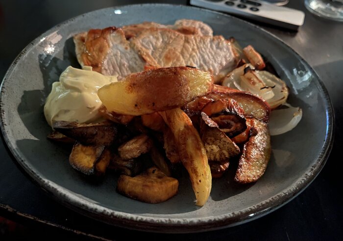 Tunnskuren fläskkotlett med ugnsrostade grönsaker och bea på en tallrik. Grönsaker inkluderar potatis, sötpotatis, och morot.