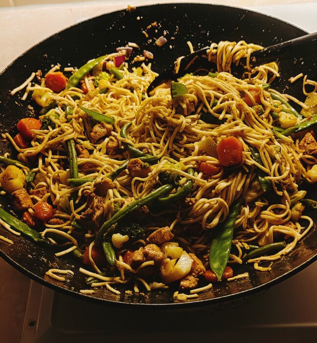 Wok med kyckling, sockerärtor, haricots verts, rödlök, blomkål, ingefära, citrongräs, äggnudlar, chili, morötter och broccoli i en stekpanna.