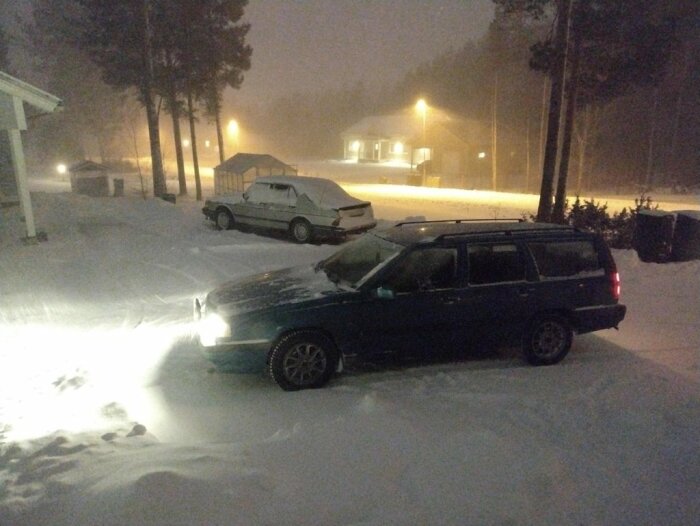 Två bilar parkerade i ett snötäckt område på natten, med strålkastarljus som lyser i mörkret.