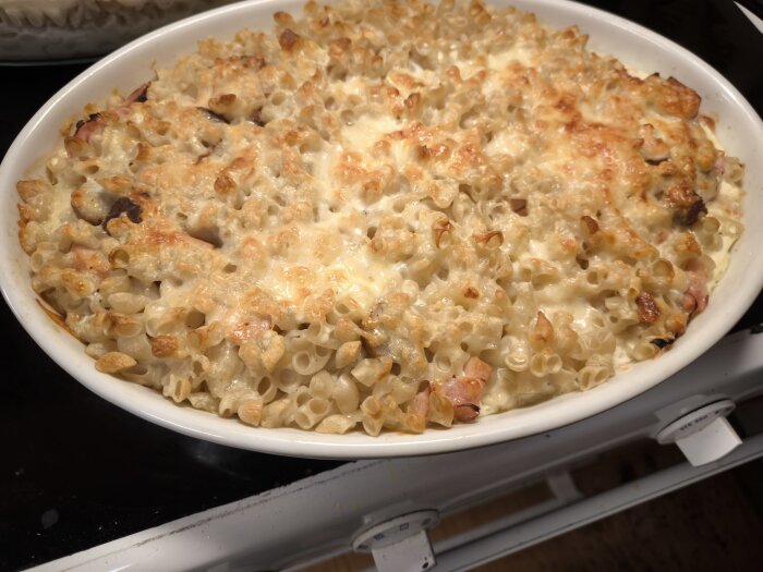 Makaronipudding i en vit ugnsform, toppad med gyllene ost, står på en spis.