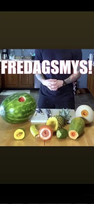 Person vid ett bord med olika frukter, inklusive en melon, ananas och grapefrukt, med texten "FREDAGSMYS!" i bakgrunden.