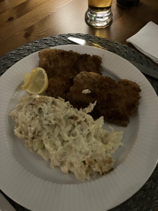 Vitkålsgratäng och schnitzel på en tallrik, dekorerad med citronklyfta.