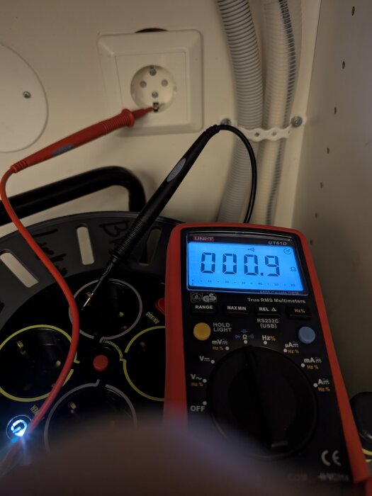 Multimeter mäter jordanslutning i eluttag, display visar motstånd på 0,9 ohm.