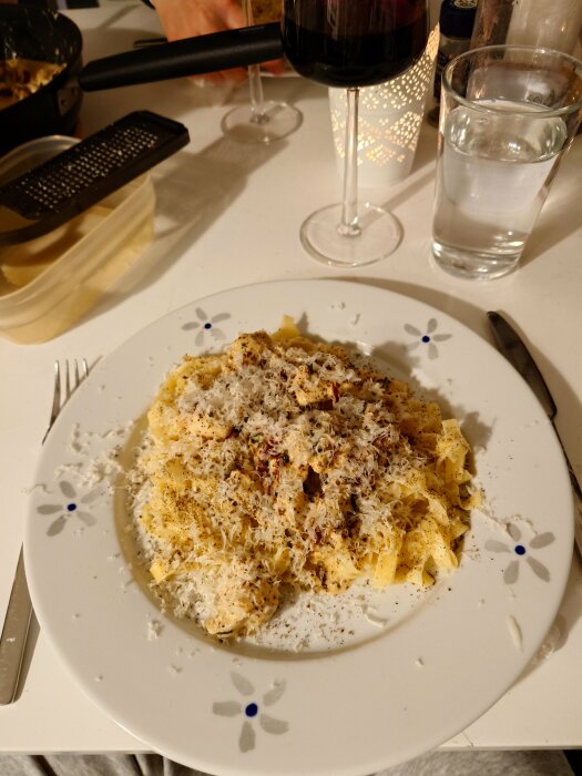 Tallrik med tagliatelle och basilikakyckling toppad med parmesan och svartpeppar, serverad med ett glas rödvin och vatten.