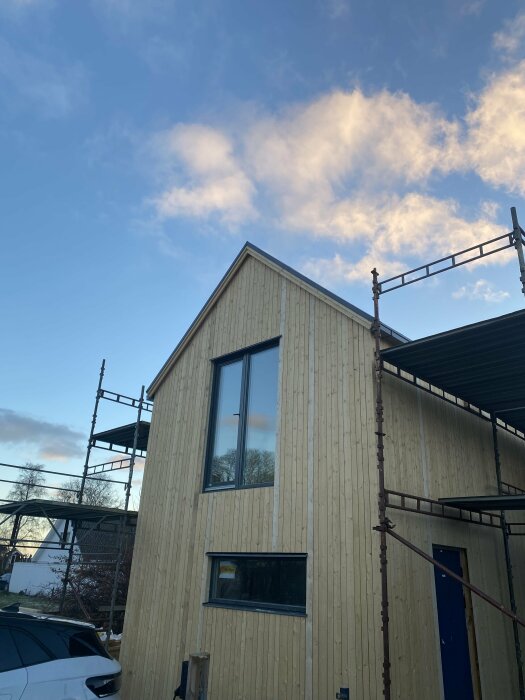 Trähus med ställning runt fasaden under rivning, himmel med moln i bakgrunden.