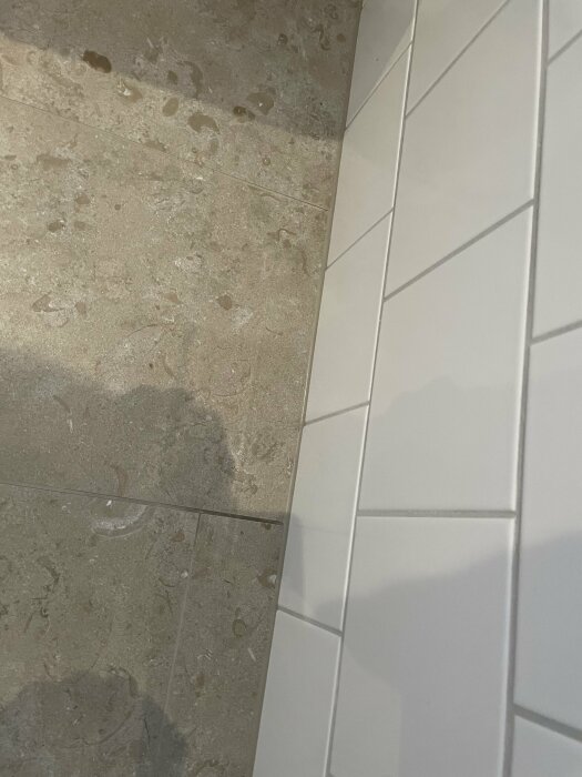 Missfärgad fog i badrumsgolvet där kakel och stenplattor möts.