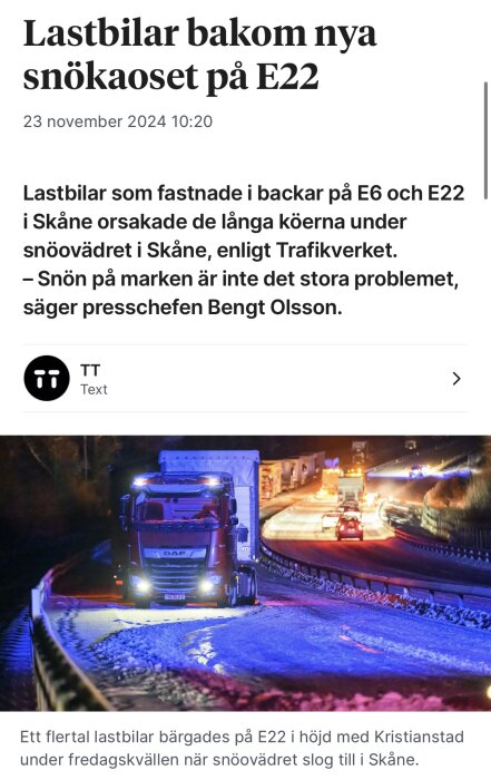 Lastbilar fast i snö på E22 under natten, med blå och röda ljus. Snöröjningsfordon syns i bakgrunden.