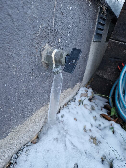 Läckande vattenutkastare mot husvägg med isbildning vid basen och snö täcker marken.